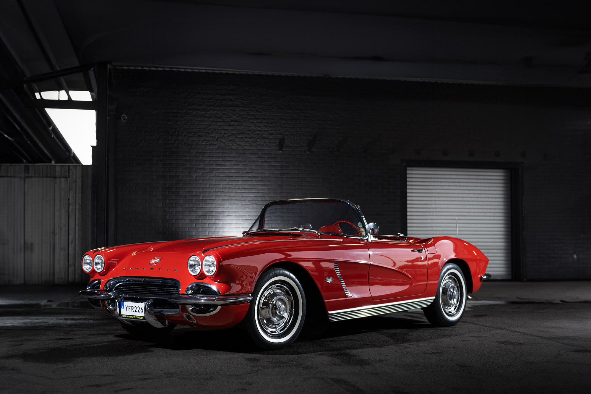 Röd Chevrolet Corvette från 1962 parkerad framför ett garage.